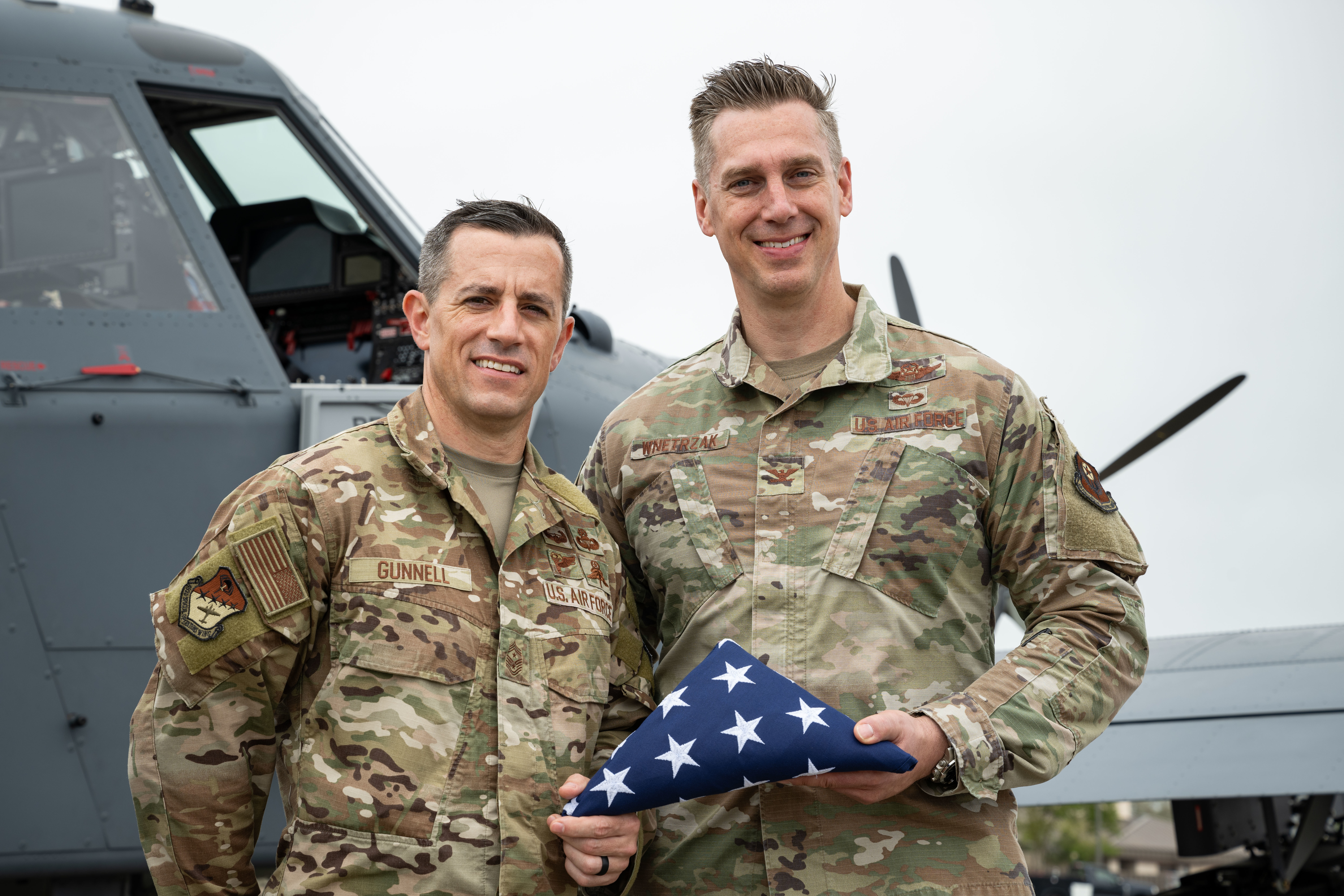 U.S. Air Force Chief Master Sgt. Thomas Gunnell, left, 492 Special Operations Wing command chief, and U.S. Air Force Col. Patrick Wnetrzak, right, 492 SOW commander, pose for a photo holding an American flag that was presented to the 492 SOW leadership team to signify the handover of the Skyraider II during the OA-1K Skyraider II arrival ceremony at Hurlburt Field, Florida, April 3, 2025. The flag presentation represents the 492 SOW’s assumption of responsibility to conduct the formal training of OA-1K Skyraider II pilots. (U.S. Air Force photo by Staff Sgt. Natalie Fiorilli)