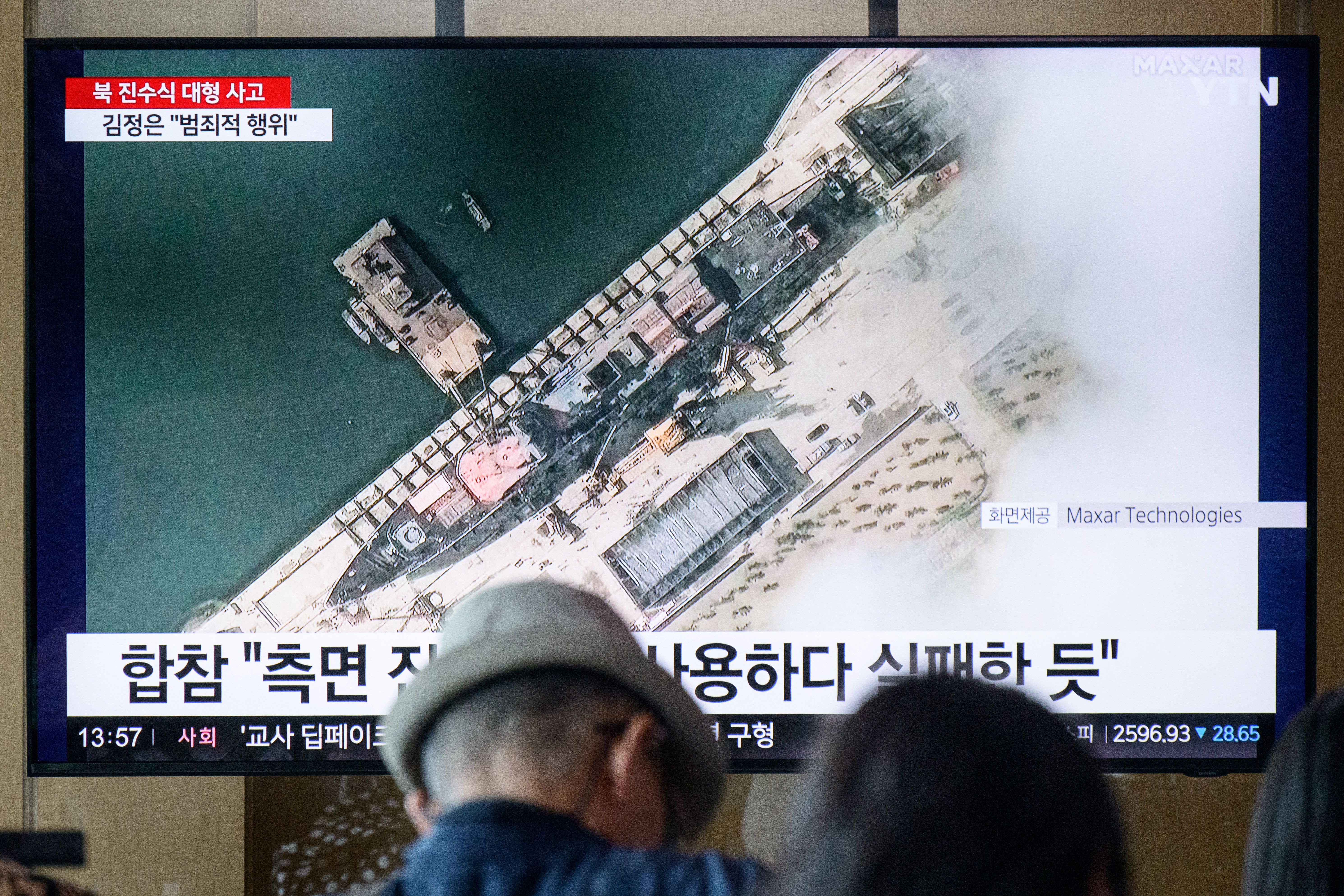 In a photo taken in Seoul on May 22, 2025, people sit near a television showing news footage with a satellite still image courtesy of Maxar Technologies showing a general view of a new North Korean warship at the harbour ahead of its launch in Chongjin. A major accident occurred at the launch ceremony for a new North Korean naval destroyer, state media reported on May 22, with leader Kim Jong Un calling the mishap a "criminal act". (Photo by ANTHONY WALLACE / AFP) (Photo by ANTHONY WALLACE/AFP via Getty Images)