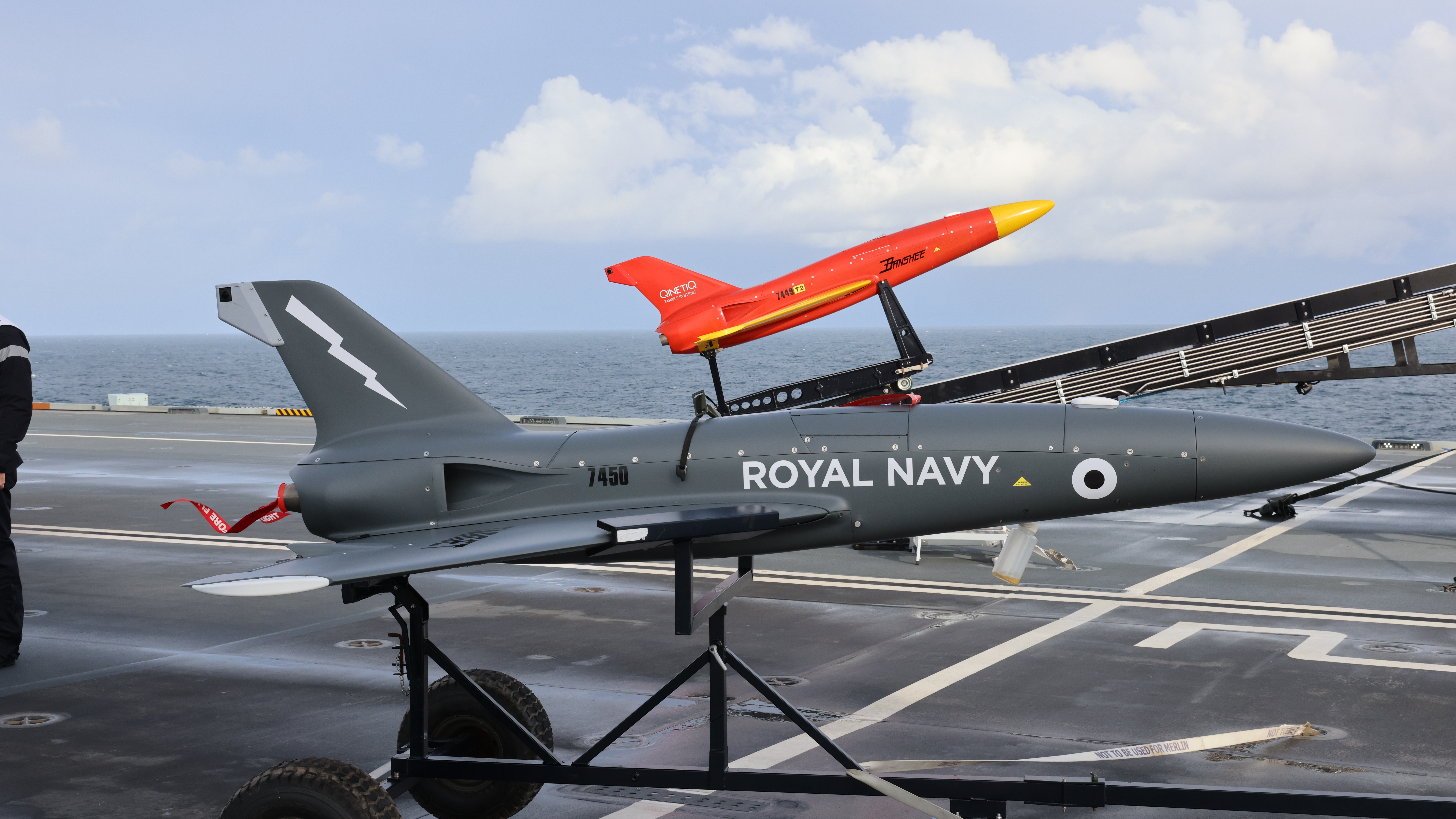 Pictured on the flight deck of HMS Prince of Wales are Banshee Jet 80 target drones (operated by 847 Sqn and QuenticQ). HMS Prince of Wales has launched target drones from her flight deck as the Royal Navy begins exploring the use of un-crewed technology on the new aircraft carriers. Developed from the original Banshee target, the twin-jet engine powered Banshee Jet 80 version was developed using knowledge and experience gained whilst operating the single jet engine variant (Banshee Jet 40) which entered service in 2010. The current version is fitted with twin 40kg thrust gas turbine engines giving a total of 80kg of static thrust. This offers an increase in the maximum straight and level airspeed of up to 180metres/second. The use of an auxiliary fuel tank ensures that endurance is similar to that of the single engine version with a typical mixed throttle mission time in excess of 45 minutes. When fitted with the patented Hot Nose the target provides a forward and side-looking IR source with output in Bands I, II and III, whilst the jet engines provide a realistic rearward looking IR signature. HMS Prince of Wales is at sea with embarked F35 Lightning jets from 207 Sqn RAF. The aircraft carrier is exercising with multiple F35s for the first time and is continuing to develop her operational capability as she prepares for her first major deployment in 2022.