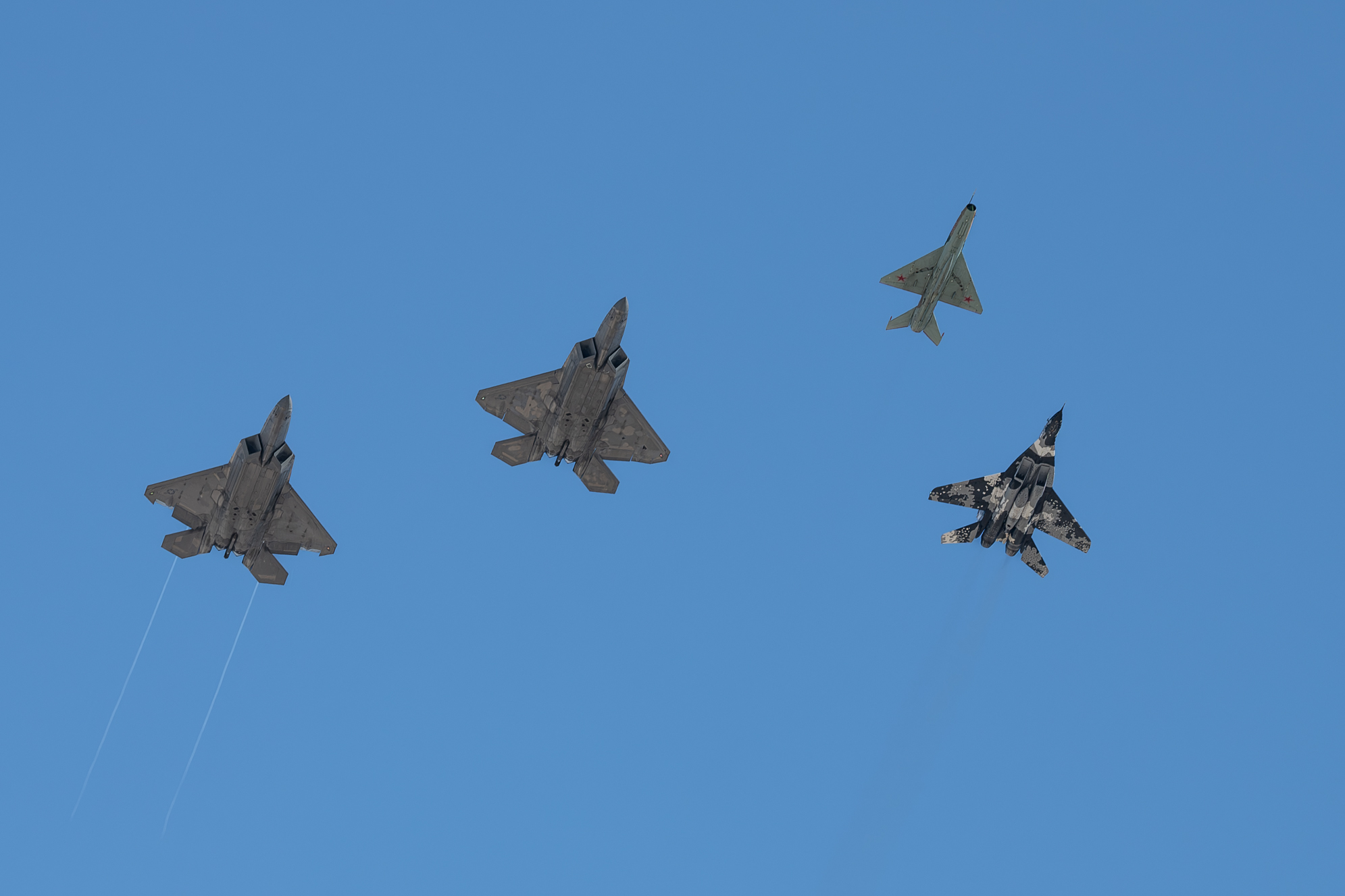 Two U.S. Air Force F-22 Raptors fly alongside a MiG-29 and a MiG-21 during a memorial flyover for Retired U.S. Air Force Col. Gail Peck at Nellis Air Force Base, Nevada, Nov. 7, 2024. Col. Peck was the first commanding officer of the 4477th TES Red Eagles, a unit that operated Soviet MiG-17s, MiG-21s and MiG-23s between 1977 and 1988 to train the US Air Force, Navy and Marine Corps pilots and weapon systems officers in air combat tactics against these foreign aircraft. (U.S. Air Force photo by William R. Lewis)