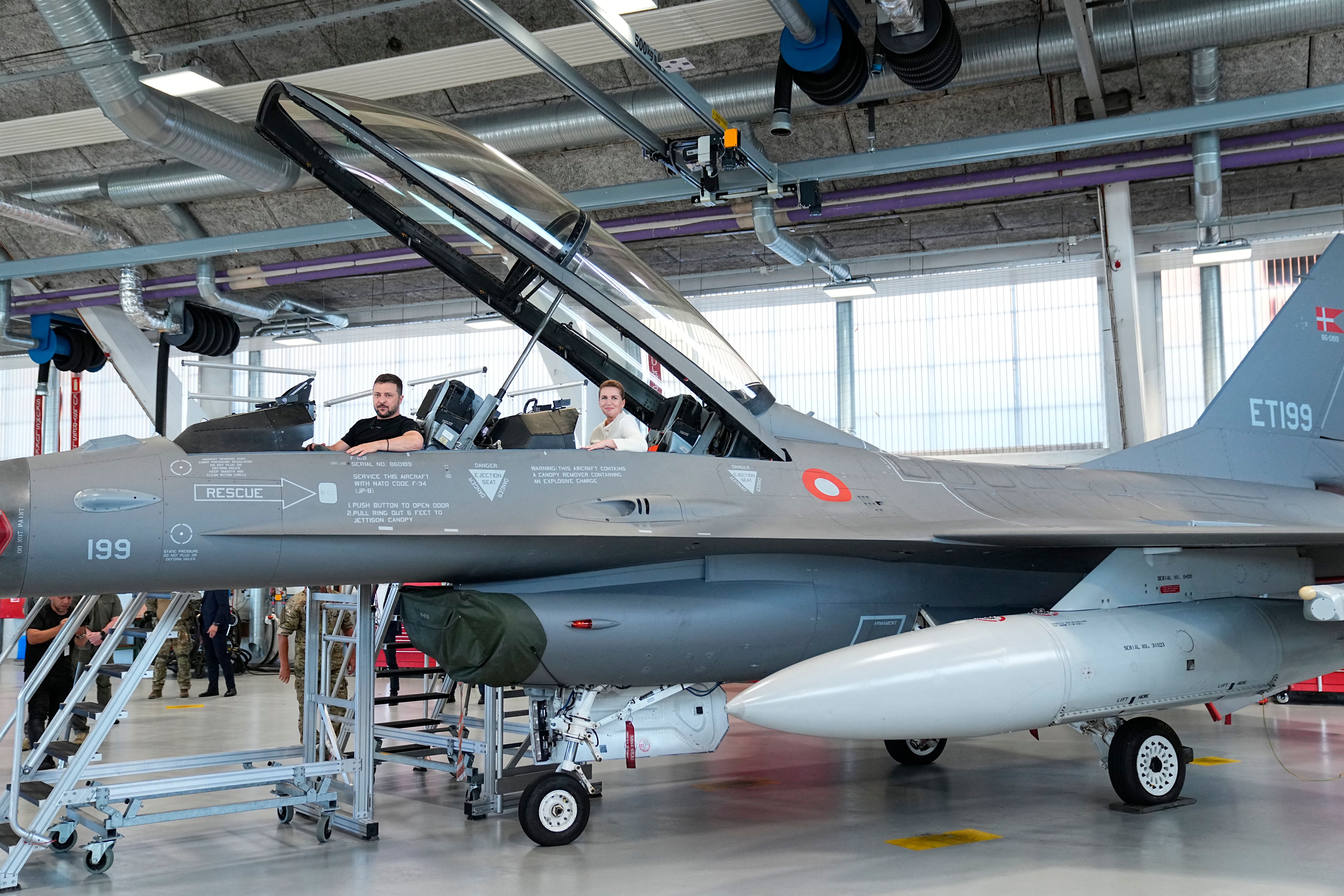 Ukrainian President Volodymyr Zelensky (L) and Danish Prime Minister Mette Frederiksen (R) react as they sit in a F-16 fighter jet in the hangar of the Skrydstrup Airbase in Vojens, northern Denmark, on August 20, 2023. Washington has told Denmark and the Netherlands that they will be permitted to hand over their F-16 fighter jets to Ukraine when the country's pilots are trained to operate them, the US State Department said on August 18, 2023. Both Denmark and the Netherlands are leading the program to train Ukraine's pilots on the F-16. (Photo by Mads Claus Rasmussen / Ritzau Scanpix / AFP) / Denmark OUT (Photo by MADS CLAUS RASMUSSEN/Ritzau Scanpix/AFP via Getty Images)