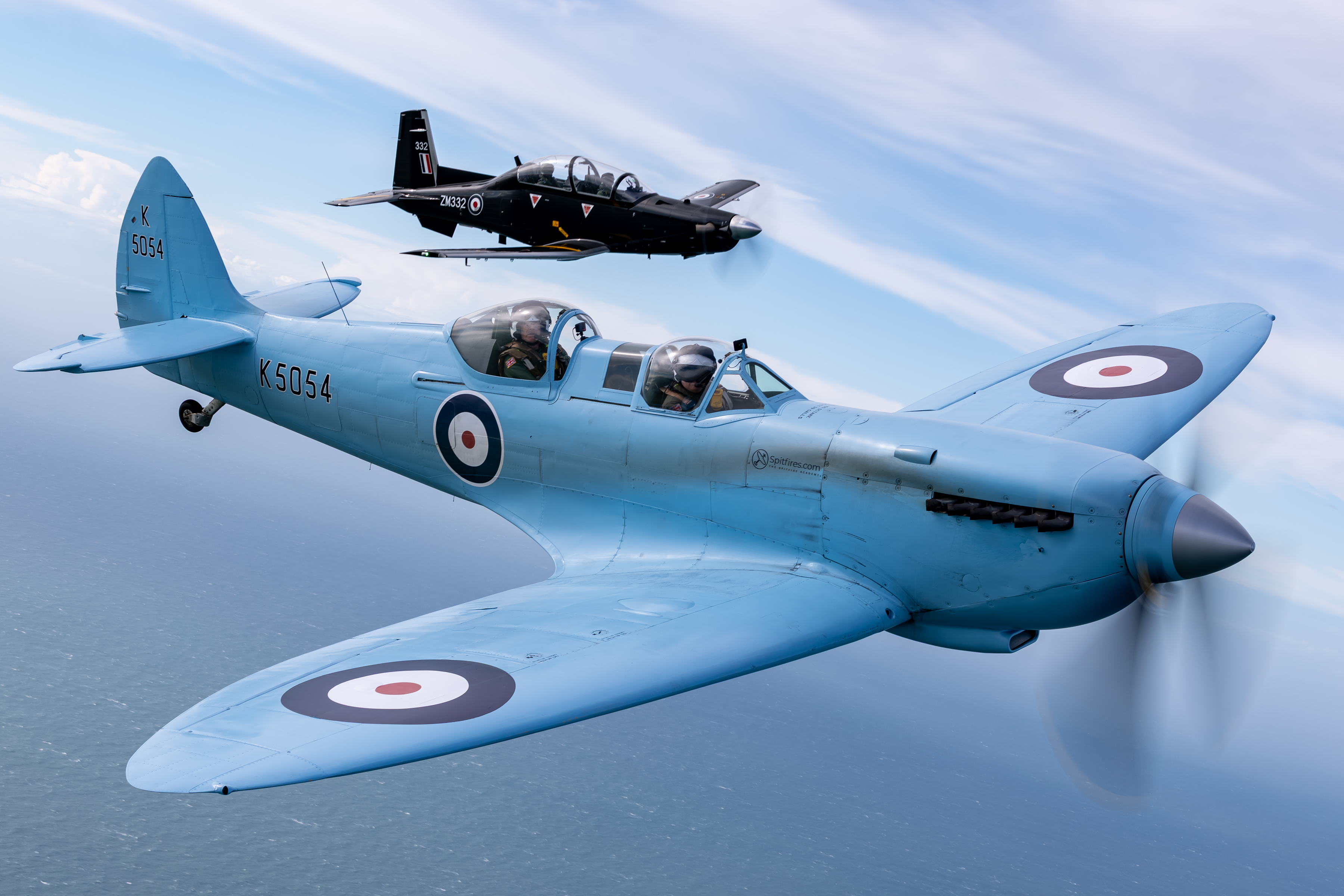 Pictured is the iconic Spitfire TR9 “K5054”, flying alongside a Texan from MOD St Athan in the UK. The sixth flight of the eagerly anticipated commemorative Spitfire90 tour has successfully left RAF Valley and landed at MOD St Athan. The commemorative SPITFIRE 90 event is celebrating 90 years of the infamous WWII aircrraft taken Wednesday 15th April 2026. SPITFIRE 90 is a collaborative commemorative event between the Royal Air Force and Spitfires.com. The nine-day event presents a unique and valuable opportunity to honour the legacy of the iconic Spitfire, celebrating its pivotal role in shaping the UK and RAF's history and inspiring future generations. It also serves to promote the modern-day RAF, showcasing its continued excellence, innovation and dedication to protecting the nation. Additionally, it has raised over £100K for RAF charities, supporting the welfare of our personnel, veterans and their families, while also providing aviation opportunities for disabled individuals. SPITFIRE 90 circumnavigates Great Britain and conducts over nine legs, each of which coordinates with modern RAF aircraft to demonstrate the progress of air power during the last nine decades. SPITFIRE 90 will operate from/ to nine UK locations: Southampton Airport, RAF Coningsby, RAF Leuchars, RAF Lossiemouth, RAF Valley, MoD St Athan, RAF St Mawgan/ Newquay Airport and Exeter Airport during the period 7–17 Apr 26.