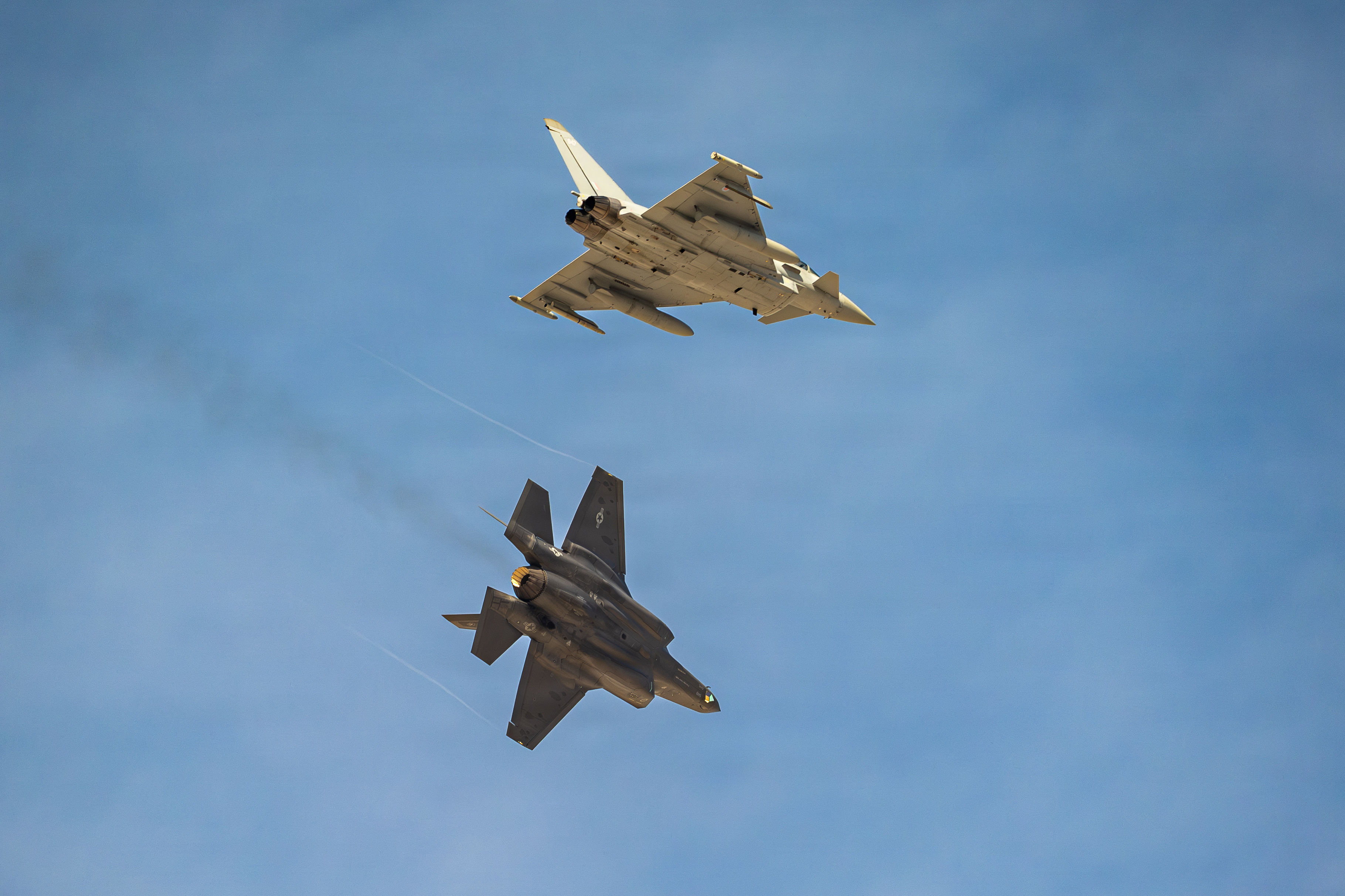 Pictured: RAF Typhoon FGR4 and a U.S. Air Force F-35A Lightning II prepare to land at Nellis Air Force Base, Nevada, Jan. 26, 2026 Exercise Red Flag is the world’s premier air combat training exercise, held annually by the United States Air Force in Nevada, consisting of the Royal Air Force (RAF), the Royal Australian Air Force (RAAF) and the United States Air Force (USAF). Exercise Red Flag 26-1 (Ex RF 26-1), running from 2 February to 14 February 2026. It provides the RAF with unparalleled training, as well as building the training strength of the Western Alliance. Ex RF 26-1 takes place over the Nevada Test and Training Range (NTTR), an expanse of more than 2.9 million acres of restricted airspace. This provides the RAF with a ‘sandbox’ which is impossible to replicate in the more congested skies of Western Europe. The RAF contribution to the exercise consisted of XI(F) Squadron Eurofighter Typhoon FGR4 fighter jets, a Voyager A330 MRTT for air-to-air refuelling and a Boeing RC-135W Rivet Joint reconnaissance aircraft. As well as over 300 UK personnel, including ground crews, engineers and intelligence officers, to ensure the high-tempo missions remain on schedule. This exercise has two forces: Blue Force (the UK and its allies), and the Red Force, who are comprised of the USAF’s elite ‘Aggressor’ Squadrons. These pilots are trained to fly using the tactics and manoeuvres of peer adversaries, flying F-16s and F-35s painted in different camouflage schemes. RAF Typhoon pilots on the exercise were predominantly from XI(Fighter) Squadron from RAF Coningsby, but pilots from several other Typhoon squadrons (such as 1(F) Sqn from RAF Lossiemouth) also participated. This was to ensure that the advancements made during the exercise are rapidly implemented across the RAF Typhoon Force.