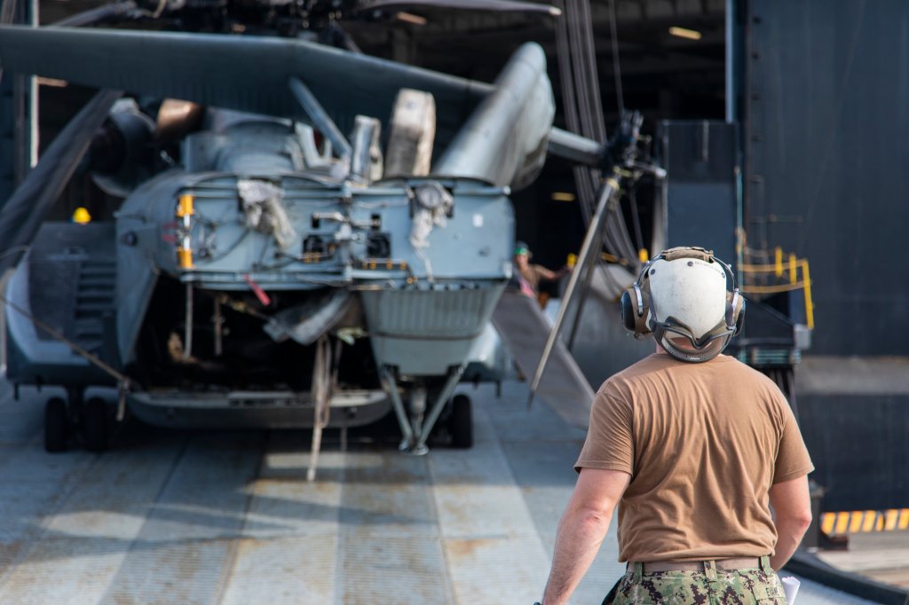 A U.S. Navy Sailor with Helicopter Mine Countermeasures Squadron 14 guides an MH-53 helicopter from a vehicle carrier ship at Marine Corps Air Station Iwakuni, Japan, Sept. 14, 2022. The Green Lake visited MCAS Iwakuni to offload an MH-53 Sea Dragon in support of Helicopter Mine Countermeasures Squadron 14 after completion of aircraft maintenance. MCAS Iwakuni is the only Marine Corps base with a collocated harbor and airfield, allowing aircraft to be rapidly transported, fixed, and redeployed. (U.S. Marine Corps photo by Cpl. Darien Wright)