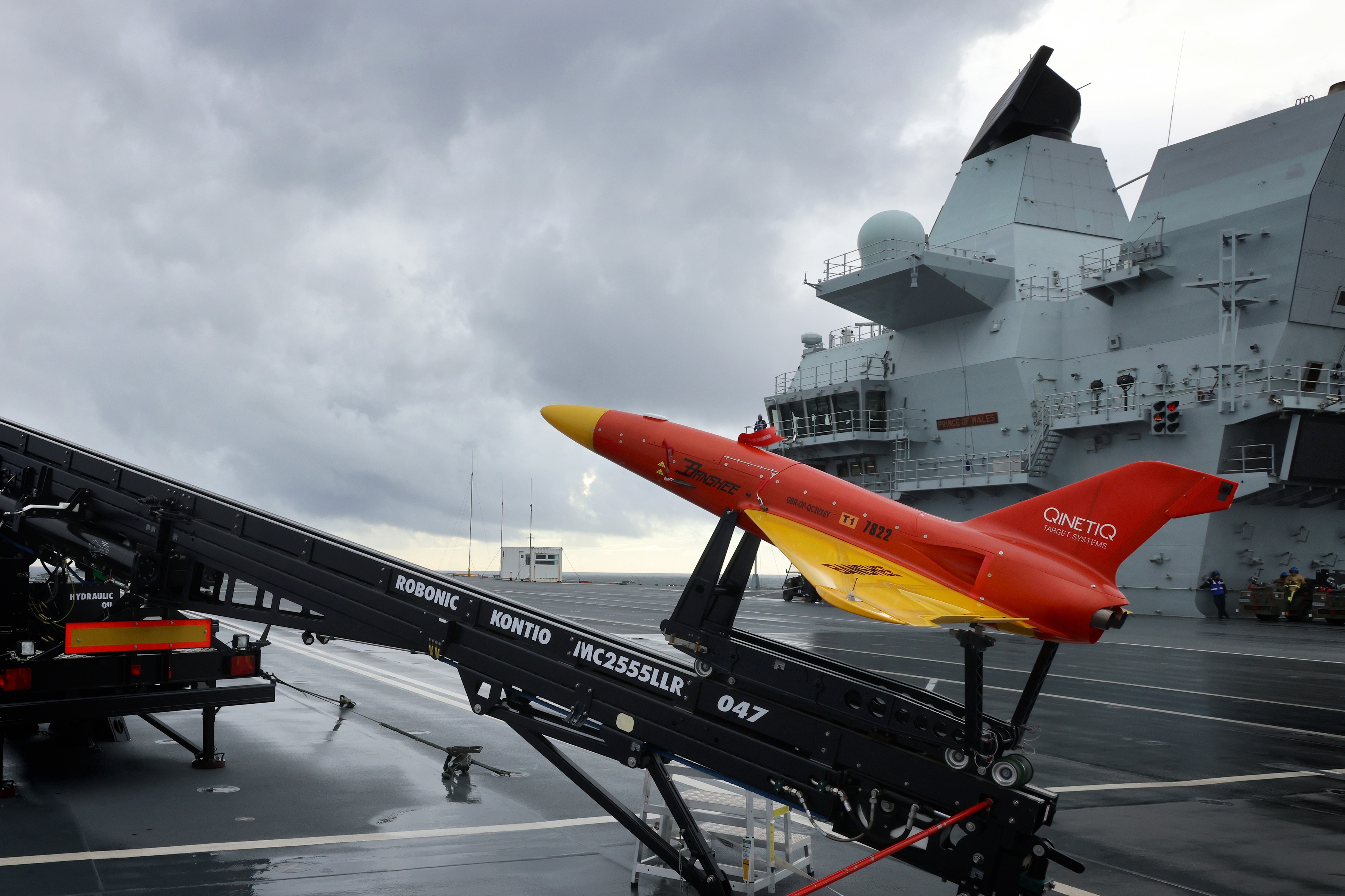 Pictured on the flight deck of HMS Prince of Wales are Banshee Jet 80 target drones (operated by 847 Sqn and QuenticQ). HMS Prince of Wales has launched target drones from her flight deck as the Royal Navy begins exploring the use of un-crewed technology on the new aircraft carriers. Developed from the original Banshee target, the twin-jet engine powered Banshee Jet 80 version was developed using knowledge and experience gained whilst operating the single jet engine variant (Banshee Jet 40) which entered service in 2010. The current version is fitted with twin 40kg thrust gas turbine engines giving a total of 80kg of static thrust. This offers an increase in the maximum straight and level airspeed of up to 180metres/second. The use of an auxiliary fuel tank ensures that endurance is similar to that of the single engine version with a typical mixed throttle mission time in excess of 45 minutes. When fitted with the patented Hot Nose the target provides a forward and side-looking IR source with output in Bands I, II and III, whilst the jet engines provide a realistic rearward looking IR signature. HMS Prince of Wales is at sea with embarked F35 Lightning jets from 207 Sqn RAF. The aircraft carrier is exercising with multiple F35s for the first time and is continuing to develop her operational capability as she prepares for her first major deployment in 2022.