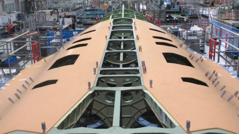 Unlike artist’s renderings, which offer few clues about scale, the factory-floor photograph includes technicians, assembly tooling, work platforms, and production fixtures that immediately provide useful reference points. Even allowing for perspective effects, the demonstrator’s center fuselage appears exceptionally broad and deep, giving the aircraft a physical presence that is difficult to appreciate in computer-generated imagery.