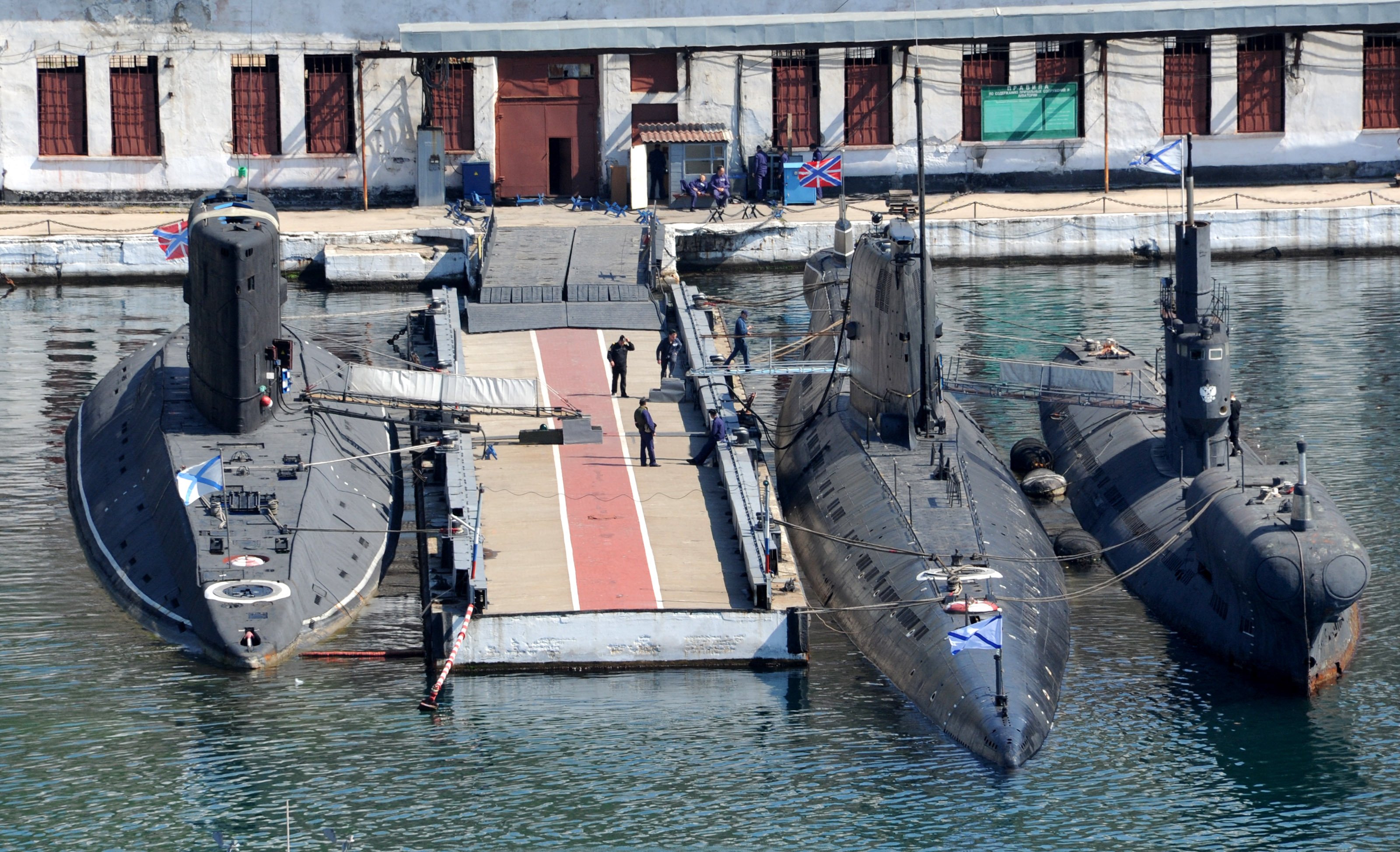 Russian naval flags are seen on the Zaporizhzhia' former Ukrainian submarine (C) moored between the Alrosa (L) and PZS-50 (R) Russian submarines in the bay of the Crimean port of Sevastopol on March 27, 2014. Ukraine's maritime forces have been severely diminished by the Russian intervention in Crimea after they lost 12 of their 17 warships to Moscow, including Ukraine's only Foxtrot-class diesel-electric submarine of the 1970s-era, the Zaporizhzhia, defence analysts Jane's said. AFP PHOTO/ VIKTOR DRACHEV (Photo by VIKTOR DRACHEV / AFP) (Photo by VIKTOR DRACHEV/AFP via Getty Images)