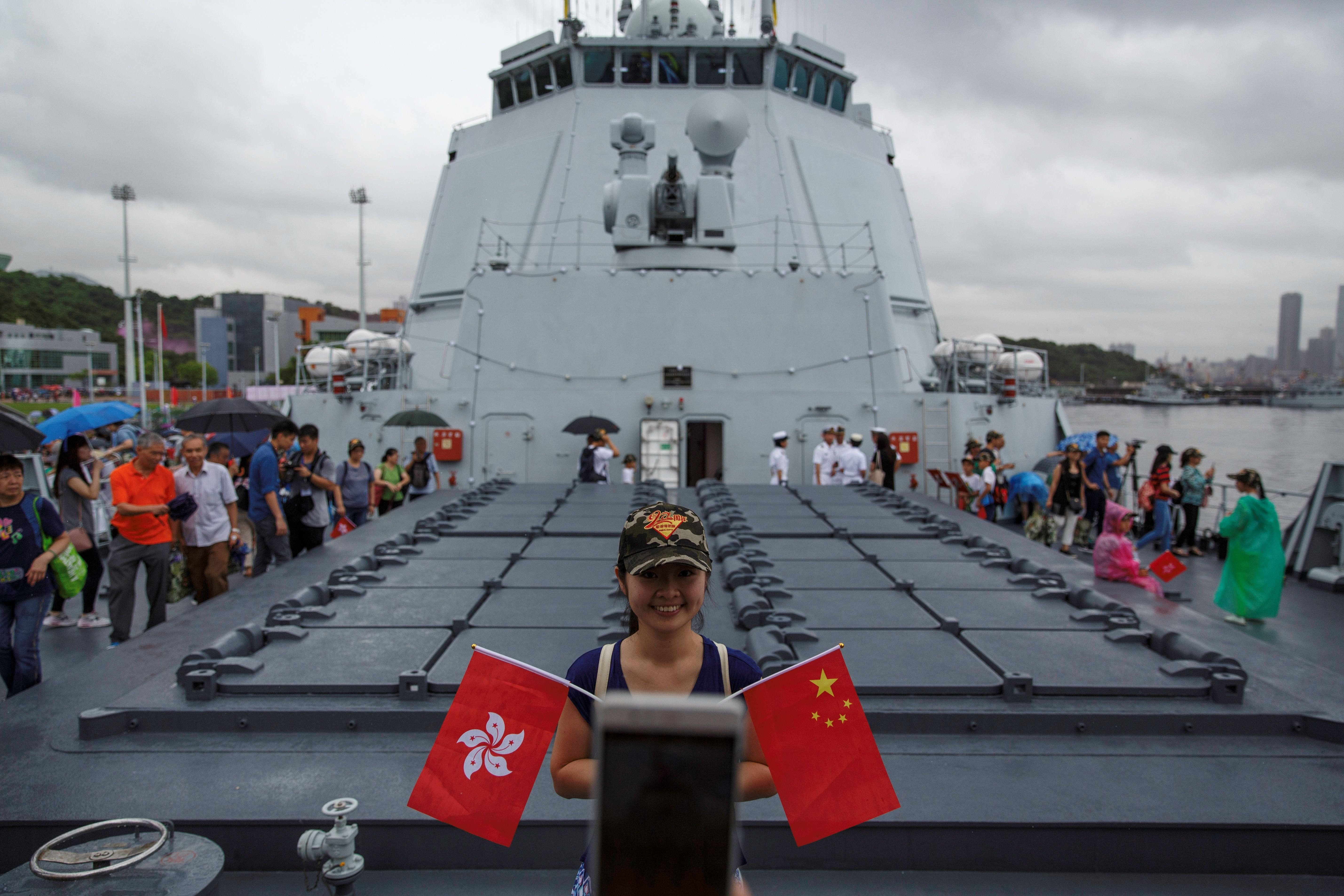A visitor poses with the Chinese (R) and Hong Kong flags on board the Yinchuan, a People's Liberation Army (PLA) Navy Type 052D destroyer, at the Ngong Shuen Chau naval base on Stonecutters Island in Hong Kong on July 8, 2017, during the PLA Hong Kong Garrison's open day held as part of 20th anniversary celebrations marking the territory's handover from Britain to China. / AFP PHOTO / TENGKU Bahar (Photo credit should read TENGKU BAHAR/AFP via Getty Images)