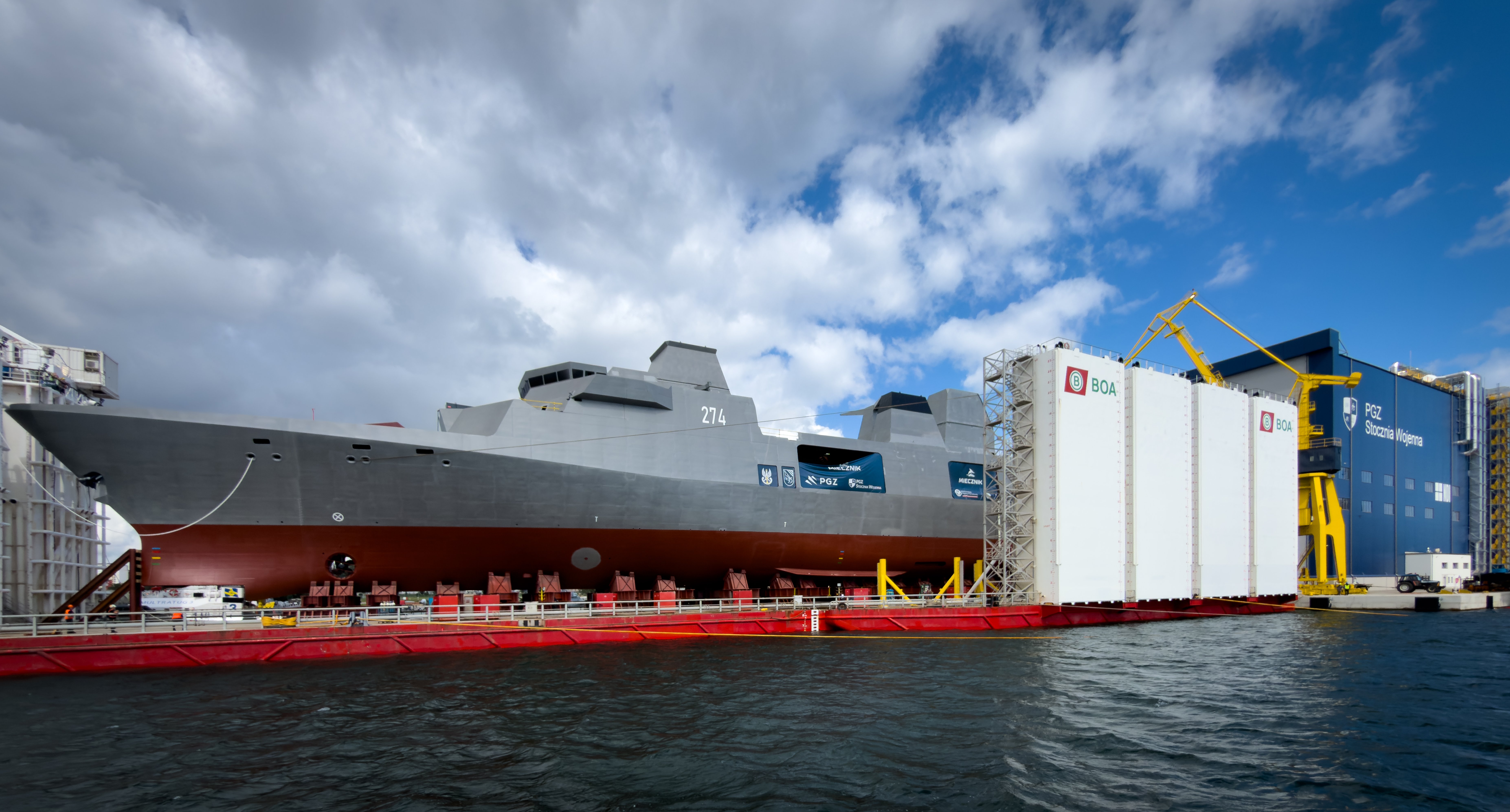 A wide view shows the future Polish Navy multipurpose frigate ORP Wicher, pennant number 274, aboard the semi-submersible heavy-lift barge BOABARGE 33 with the PGZ Stocznia Wojenna Hull Hall visible behind it in Gdynia, Poland, on August 11, 2026. The frigate was assembled and integrated inside the hall before being rolled out and positioned on the barge for its christening and launch. (Photo by Mateusz Wlodarczyk/NurPhoto via Getty Images)