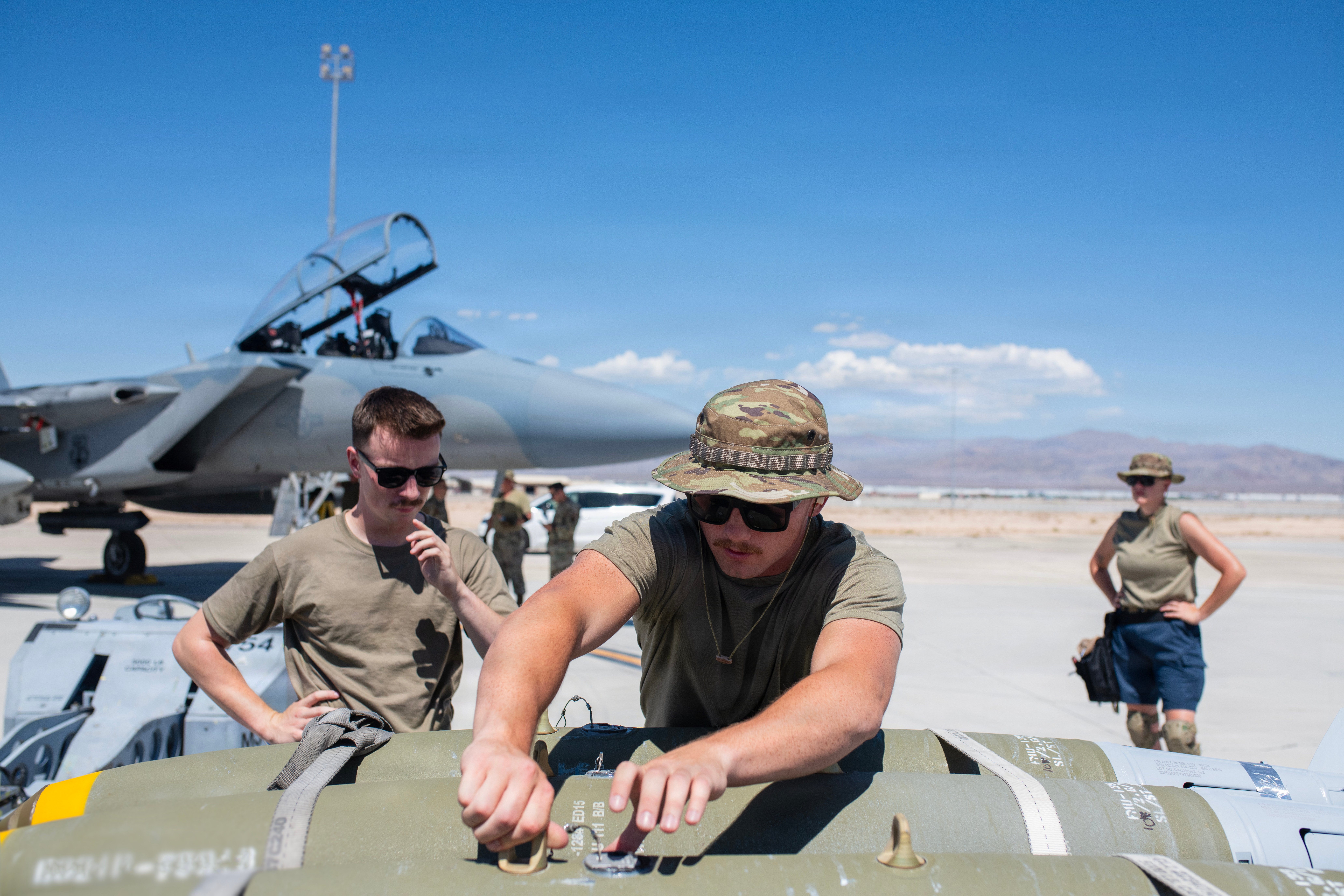 U.S. Air Force Staff Sgt. Parker Mayhew (center), a weapons loader assigned to the 142nd Aircraft Maintenance Squadron, prepares a bomb to be loaded onto an F-15EX Eagle II aircraft as U.S. Air Force Senior Airman Alexander Walker (left) looks on, August 26, 2026, Nellis Air Force Base, Nevada. The 142nd Wing’s fleet of F-15EXs operated out of Nellis AFB for three weeks in late August and early September in support of the U.S. Air Force’s Weapons Instructor Course (WIC). During this time, the unit hit a historical milestone, dropping live bombs from operational F-15EXs for the first time. (U.S. Air National Guard photo by Master Sgt. Steph Sawyer)