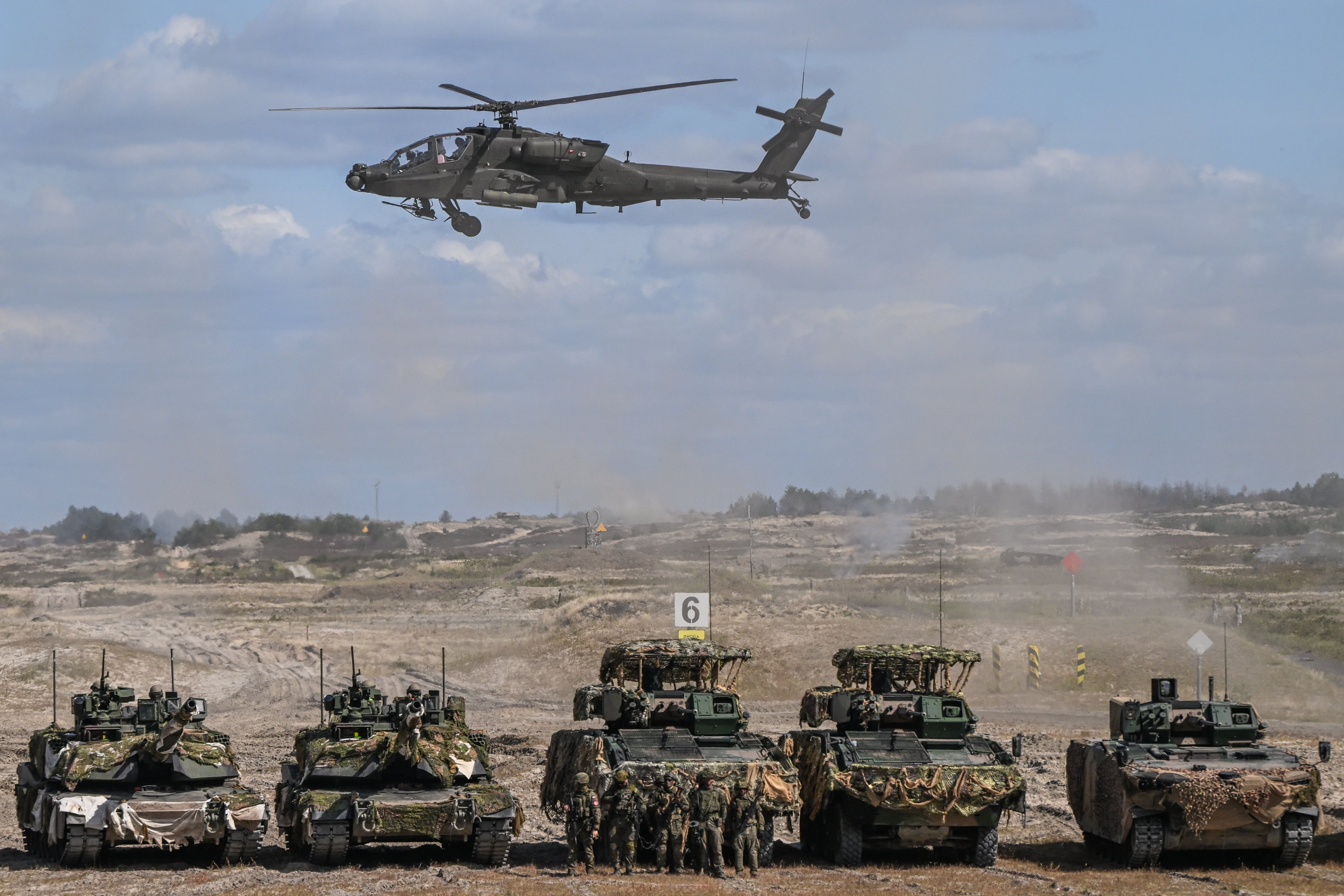 NOWA DEBA, POLAND - SEPTEMBER 7: A Boeing AH-64 Apache attack helicopter performs low-altitude tactical maneuvers over a massive static line of advanced hardware, including two camouflaged M1A1 Abrams main battle tanks, two KTO Rosomak 8x8 wheeled vehicles with ZSSW-30 turrets, and a Borsuk tracked infantry fighting vehicle, during a combat presentation at the Land Forces Training Center in Nowa Deba, Subcarpathian Voivodeship, Poland, on September 7, 2026. This high-profile combined-arms presentation, organized as part of the 27th Polish Armed Forces Exhibition directly leading into the 34th International Defence Industry Exhibition (MSPO Kielce), demonstrated the tight operational synergy between Poland's newest heavy armor, advanced infantry fighting platforms, and close-air support aviation, witnessed by foreign military delegations from over 20 countries observing Poland's premier weapon systems. (Photo by Artur Widak/NurPhoto via Getty Images)