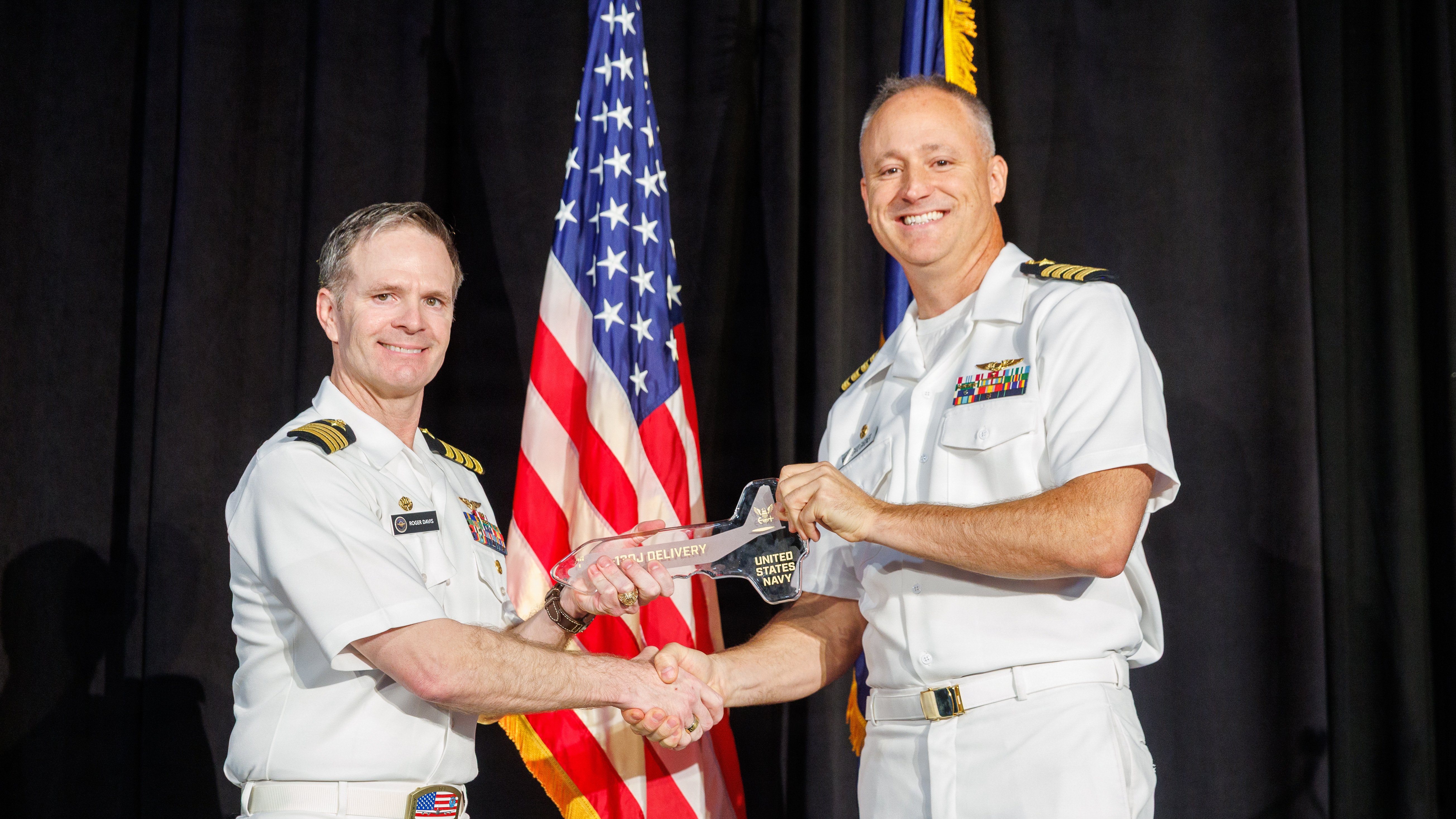 Capt. Roger Davis, left, Airborne Strategic Command, Control and Communications program manager (PMA-271), presents a ceremonial key to Capt. David Gardner, commodore of Strategic Communications Wing 1 (SCW 1), during the C-130J-30 delivery ceremony Oct. 15, 2026 in Marietta, Georgia. The symbolic handover marks the transition of the new airframe into the next phase of mission-system modification, ground testing and developmental flight testing, laying the foundation to field the future E-130J “Phoenix II.” (Photo courtesy of Lockheed Martin by Thinh D. Nguyen)