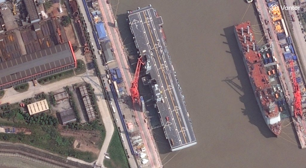The Type 076 amphibious assault ship Sichuan at the Hudong-Zhonghua shipyard on October 10, 2026. What is widely assessed to be a mothership for large uncrewed underwater vehicles (UUV) is also seen at right. Satellite image ©2026 Vantor