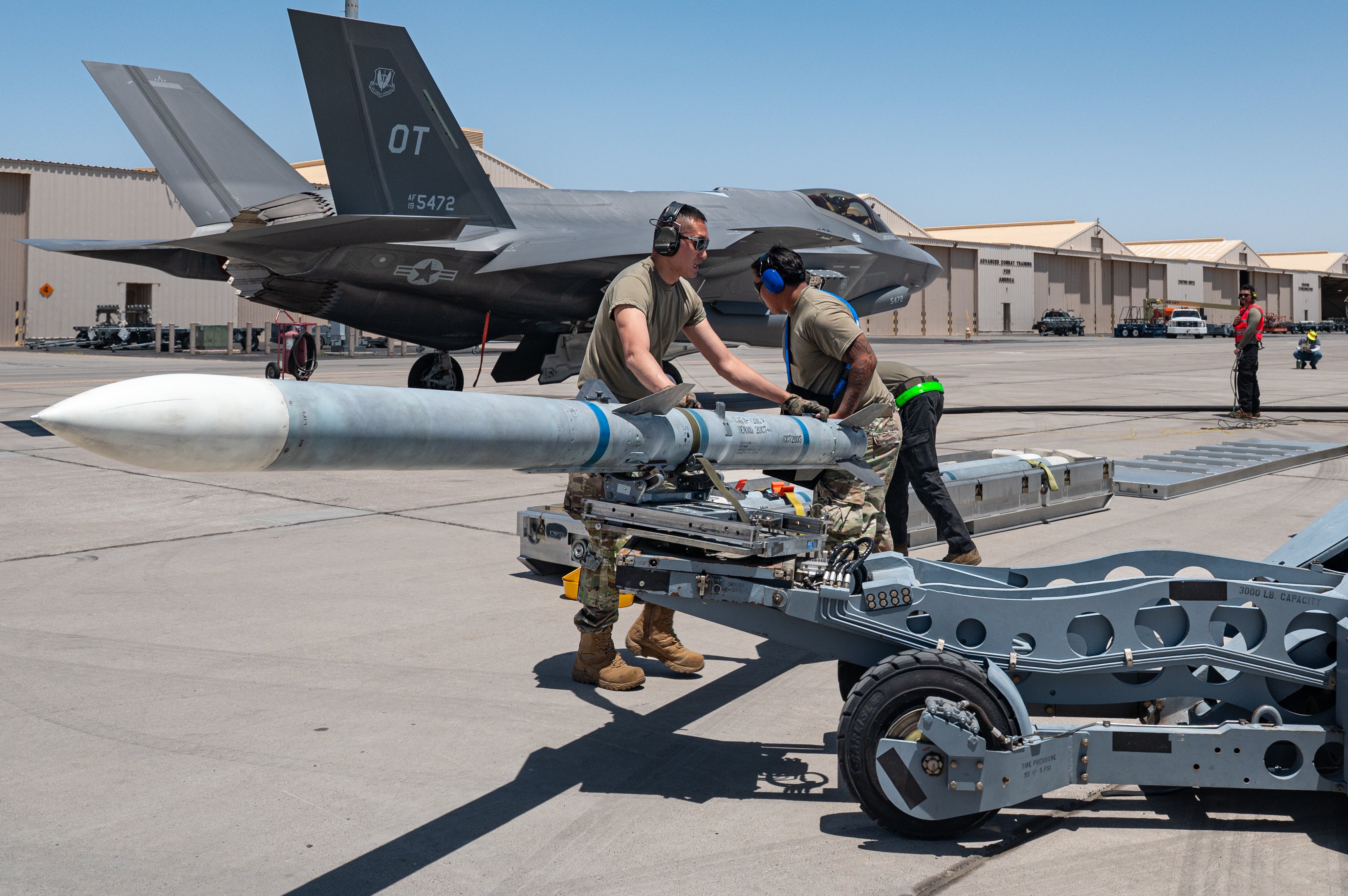 U.S. Air Force Staff Sgt. Andrew Wilson, left, a weapons load crew chief, and Senior Airman Anthony Silva, a weapons load crew member, assigned to the 57th Aircraft Maintenance Squadron’s Bolt Aircraft Maintenance Unit, secure a munition onto a bomb lift truck during a hot integrated combat turn (ICT) exercise at Nellis Air Force Base, Nevada, June 23, 2025. During hot ICTs, four AIM-120 Advanced Medium-Range Air-to-Air Missiles are loaded onto an F-35 Lightning II while the aircraft is simultaneously refueled with its engines running. (U.S. Air Force photo by William R. Lewis)