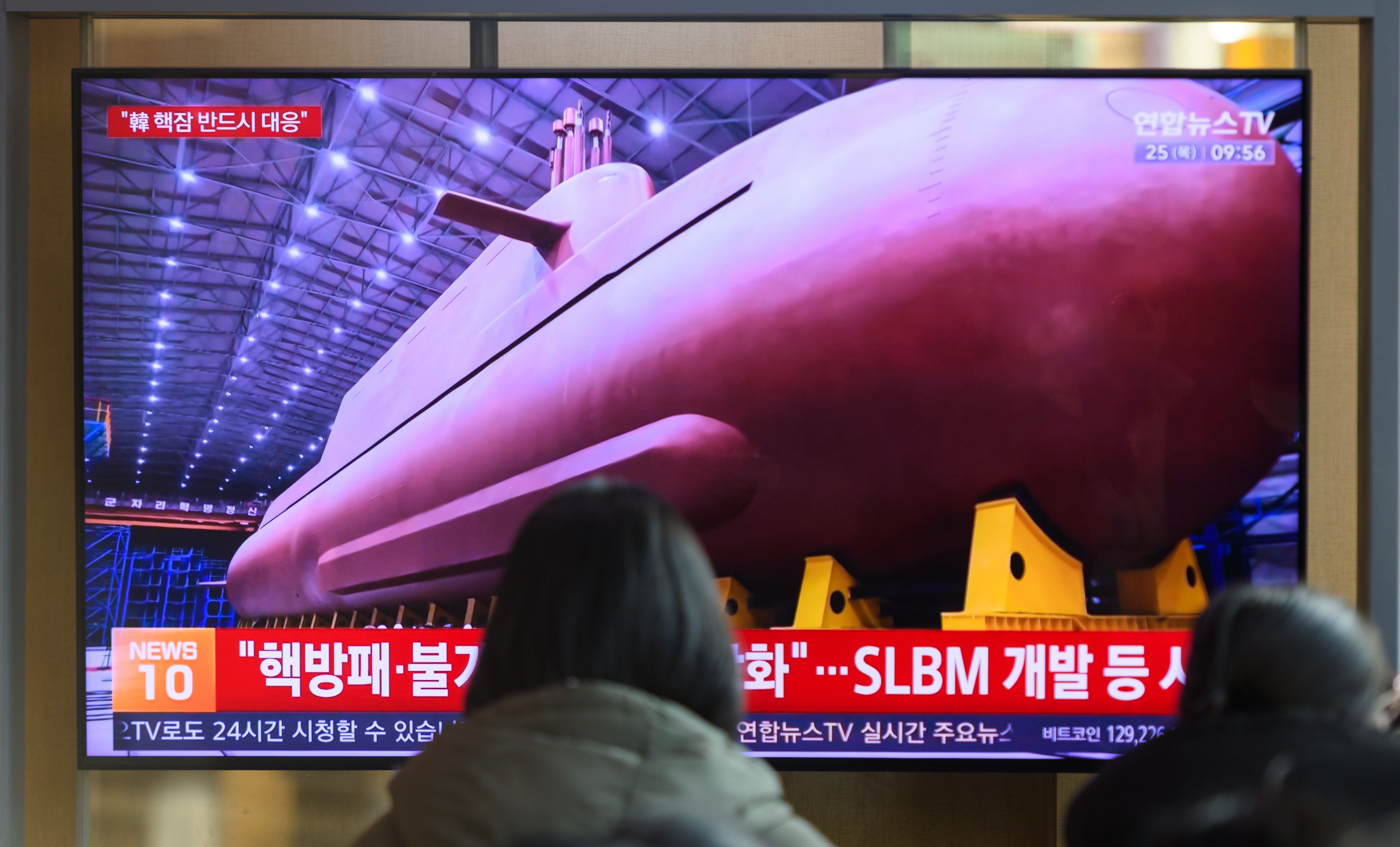 SEOUL, SOUTH KOREA - 2025/12/25: People seen looking at a 24-hour Yonhap news TV broadcast at Seoul Railway Station showing news broadcast that shows North Korean leader Kim Jong Un veiling manufacturing site of an 8,700-tonnage nuclear-powered strategic guided missile submarine at an undisclosed location. North Korean leader Kim Jong Un has said South Korea's plan to build nuclear-powered submarines will