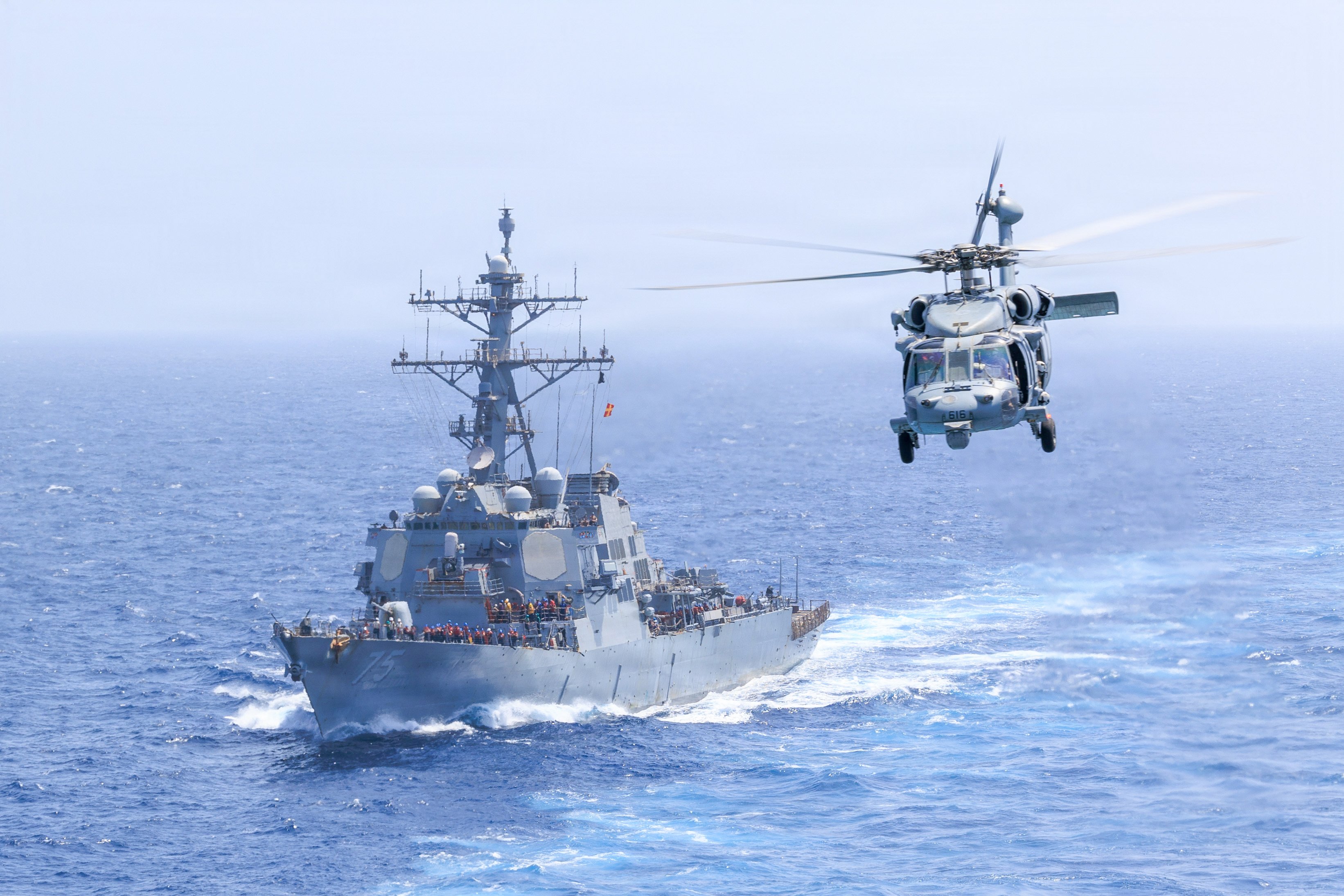 Arleigh Burke-class guided-missile destroyer USS Donald Cook (DDG 75) sails while an MH-60S Sea Hawk, attached to Helicopter Sea Combat Squadron (HSC) 5, flies alongside Nimitz-class aircraft carrier USS George H.W. Bush (CVN 77), June 18, 2026. USS George H.W. Bush is deployed to the U.S. 5th Fleet area of operations to support maritime security and stability in the Middle East. (U.S. Navy photo)